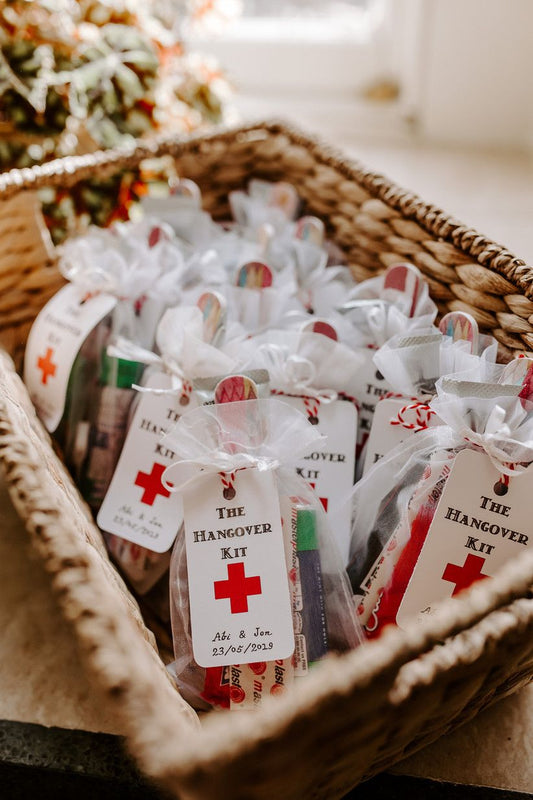 A wicker basket filled with white hanging tags with red strings and hangover kit text, presumably as a gift for a bridal shower or wedding.